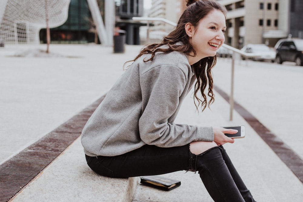 La donna si siede sul marciapiede tenendo lo smartphone mentre sorride