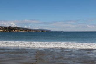 A charming seaside bungalow with a view of gentle waves and blue hills in the background.