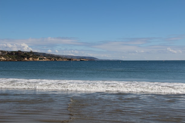 A charming seaside bungalow with a view of gentle waves and blue hills in the background.
