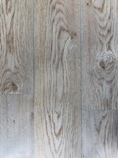 Natural wood planks with distinct grain patterns and a light brown hue. The texture shows linear and swirling grain designs, indicating a polished wooden surface.