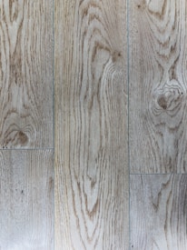Natural wood planks with distinct grain patterns and a light brown hue. The texture shows linear and swirling grain designs, indicating a polished wooden surface.