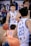 A basketball player in a white and blue jersey with the number 10 dribbles the ball on the court, surrounded by several other players. The focus is on the player with a determined expression, while the crowd and other players are slightly blurred, capturing the movement and intensity of the game.