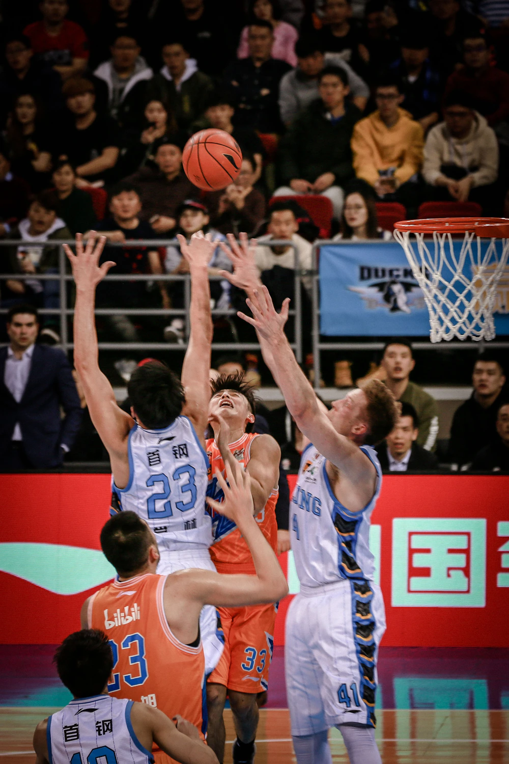 Basketball players competing for the ball in a crowded indoor arena