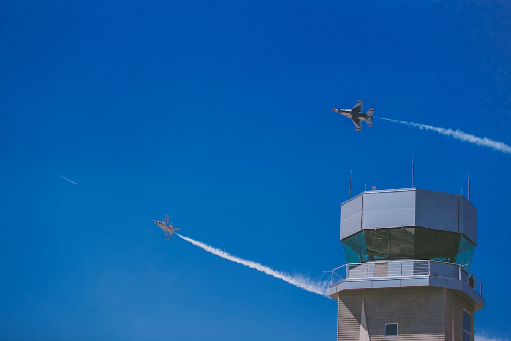 Dois aviões a jato sobrevoando o prédio cinza durante o dia