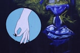 A stylized illustration features a hand with black fingernails, positioned against a light blue circular background. Adjacent to it is an abstract, blue-colored form resembling a chalice or goblet, surrounded by dark green and black brushstrokes.