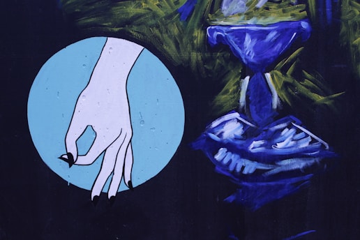 A stylized illustration features a hand with black fingernails, positioned against a light blue circular background. Adjacent to it is an abstract, blue-colored form resembling a chalice or goblet, surrounded by dark green and black brushstrokes.