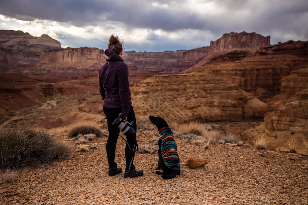 dog looking up on woman wearing black hoodie looking at brown canyon hills