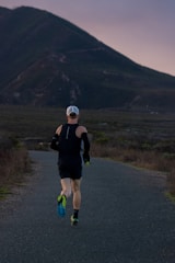 An athlete running along a mountain trail at dawn, muscles engaged and form perfect in natural light.