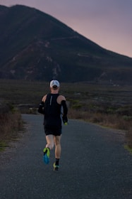 woman jogging on gray road across mountain during daytime