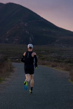 woman jogging on gray road across mountain during daytime