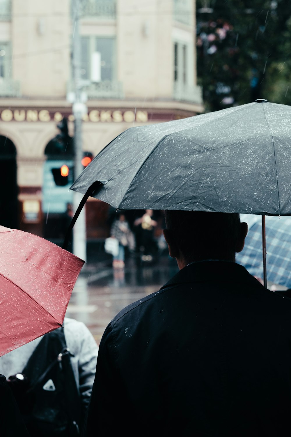 Fotografía de enfoque selectivo de hombre usando paraguas de pie detrás de la persona que usa bacpack negro