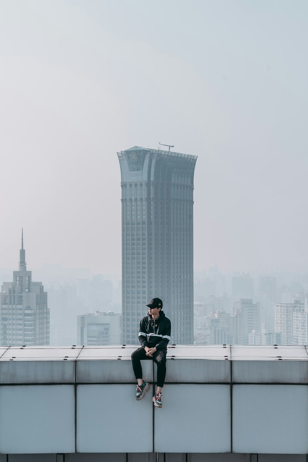 man in black coat sitting on concrete fence near concrete building