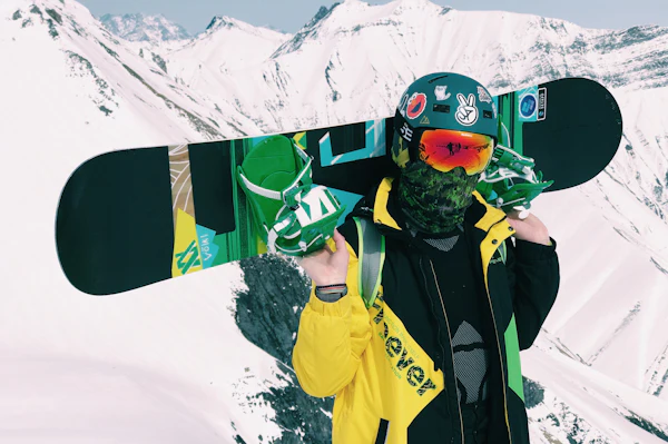 Un snowboardeur, la planche posée sur les épaules.