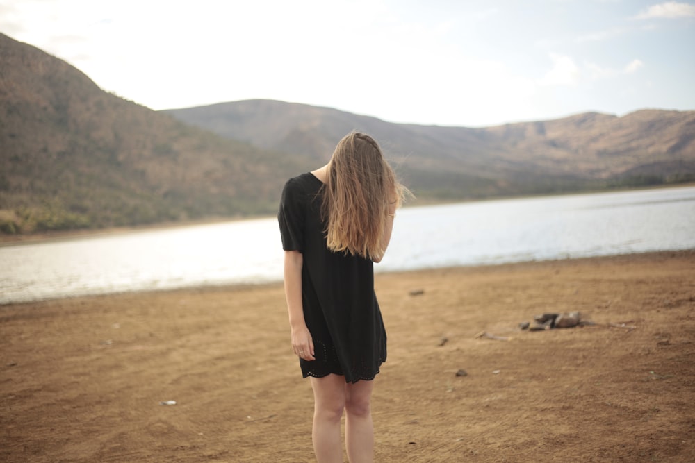 Mujer en vestido negro de pie frente al lago