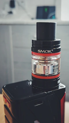 A stylish vape device resting on a wooden table with Udaipur cityscape softly blurred in the background.