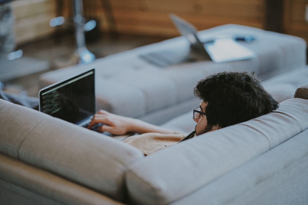 Mann, der auf der Couch liegt, während er einen Laptop benutzt