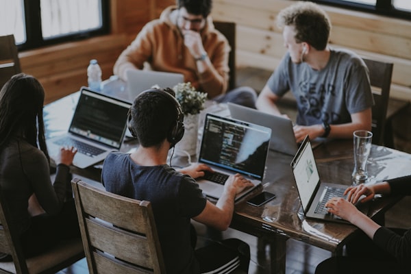 Photo of five people sitting around a table with laptops. Some have headphones.