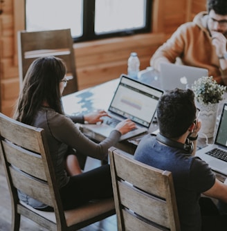 selective focus photography of woman and man using MacBook Pro on table