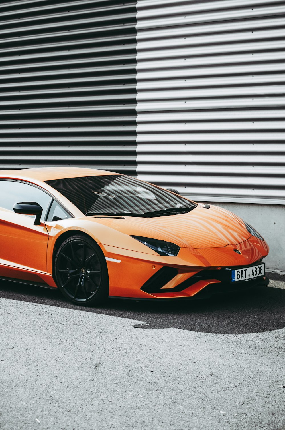 Coupé deportivo Lamborghini naranja estacionado cerca de una pared corrugada durante el día