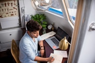 A freelancer writing notes while working on a laptop at a cozy desk.