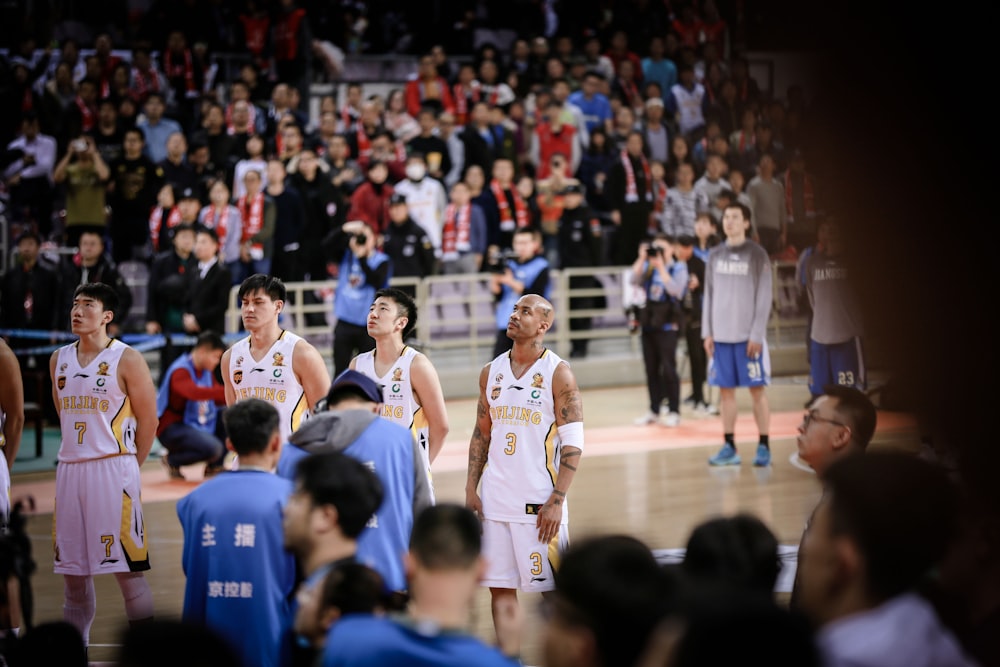 four basketball players forming a line while standing on court surrounded by crowd