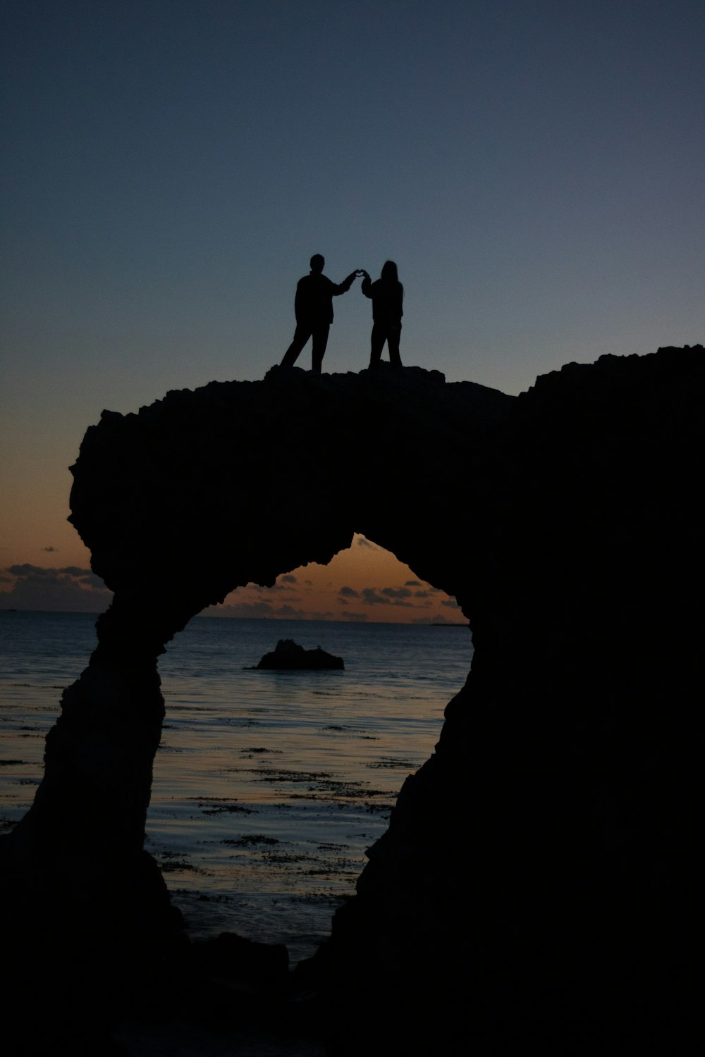 silhouette of two persons atop a rock formation near the ocean