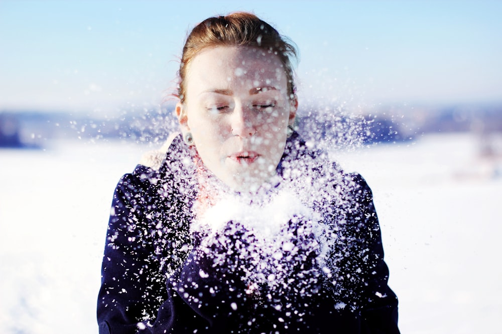 femme en veste noire soufflant la neige