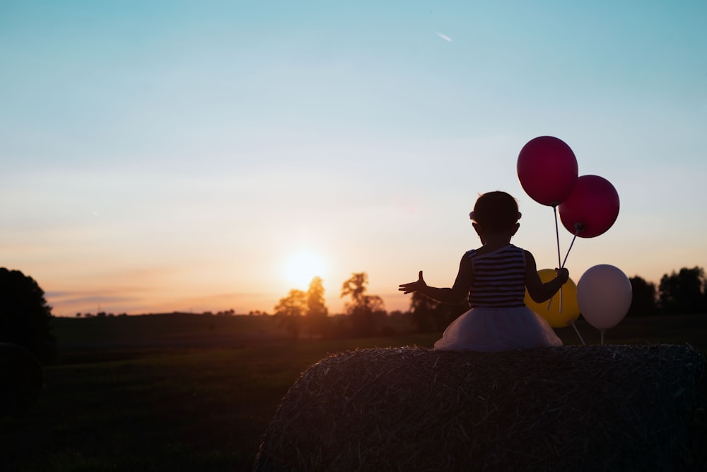 Muchacha sosteniendo cuatro globos de colores variados durante la puesta del sol