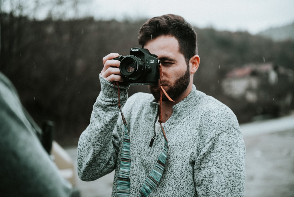 photographie sélective de mise au point d’un homme tenant un appareil photo reflex numérique