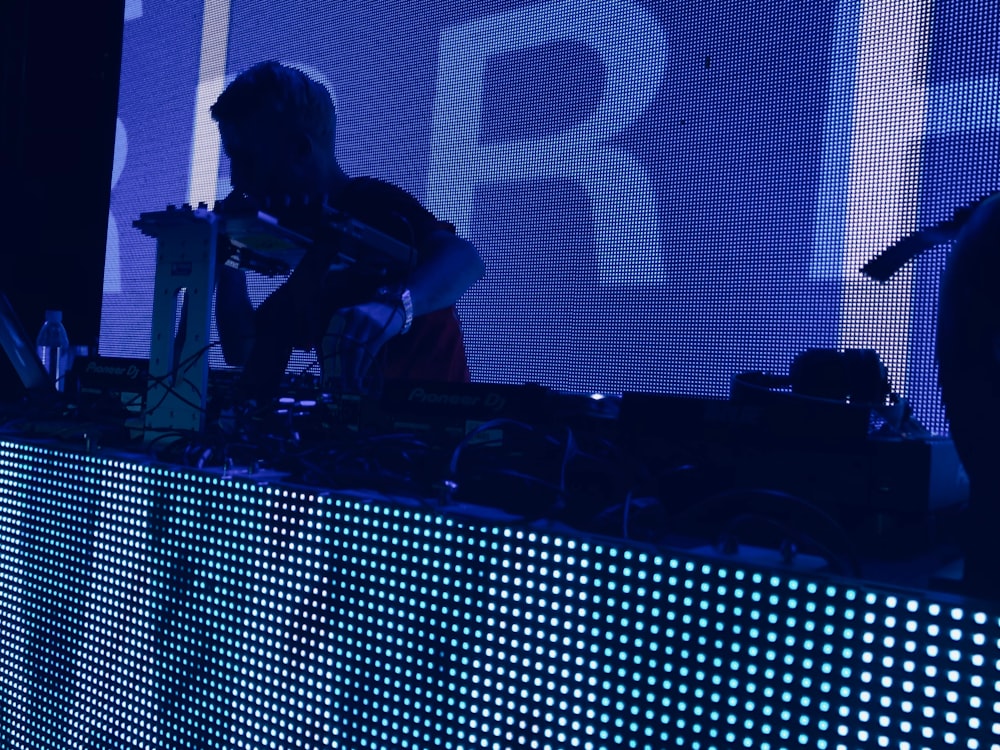 man wearing t-shirt holding DJ mixer inside dark room