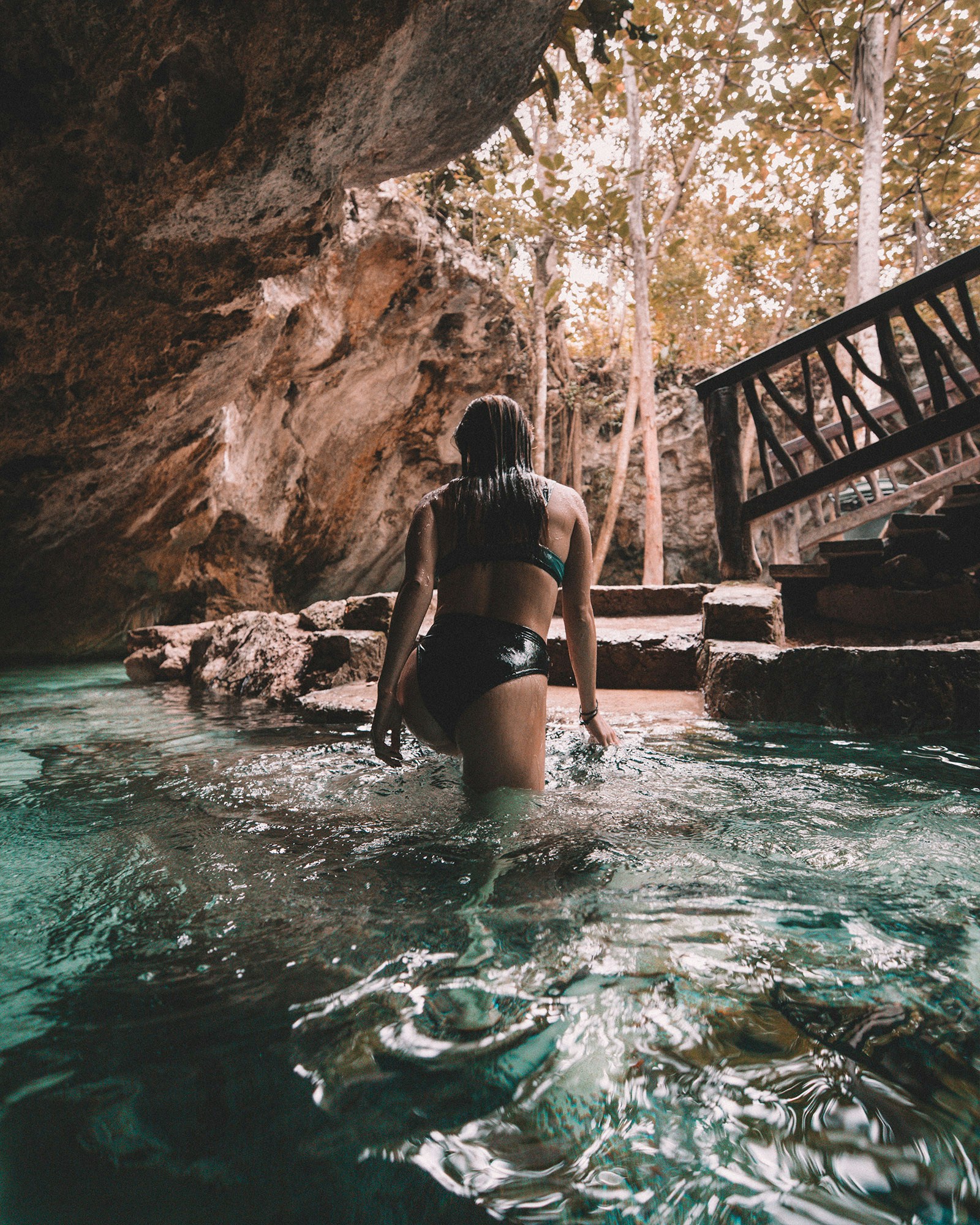 woman in bikini walking out of water inside cave