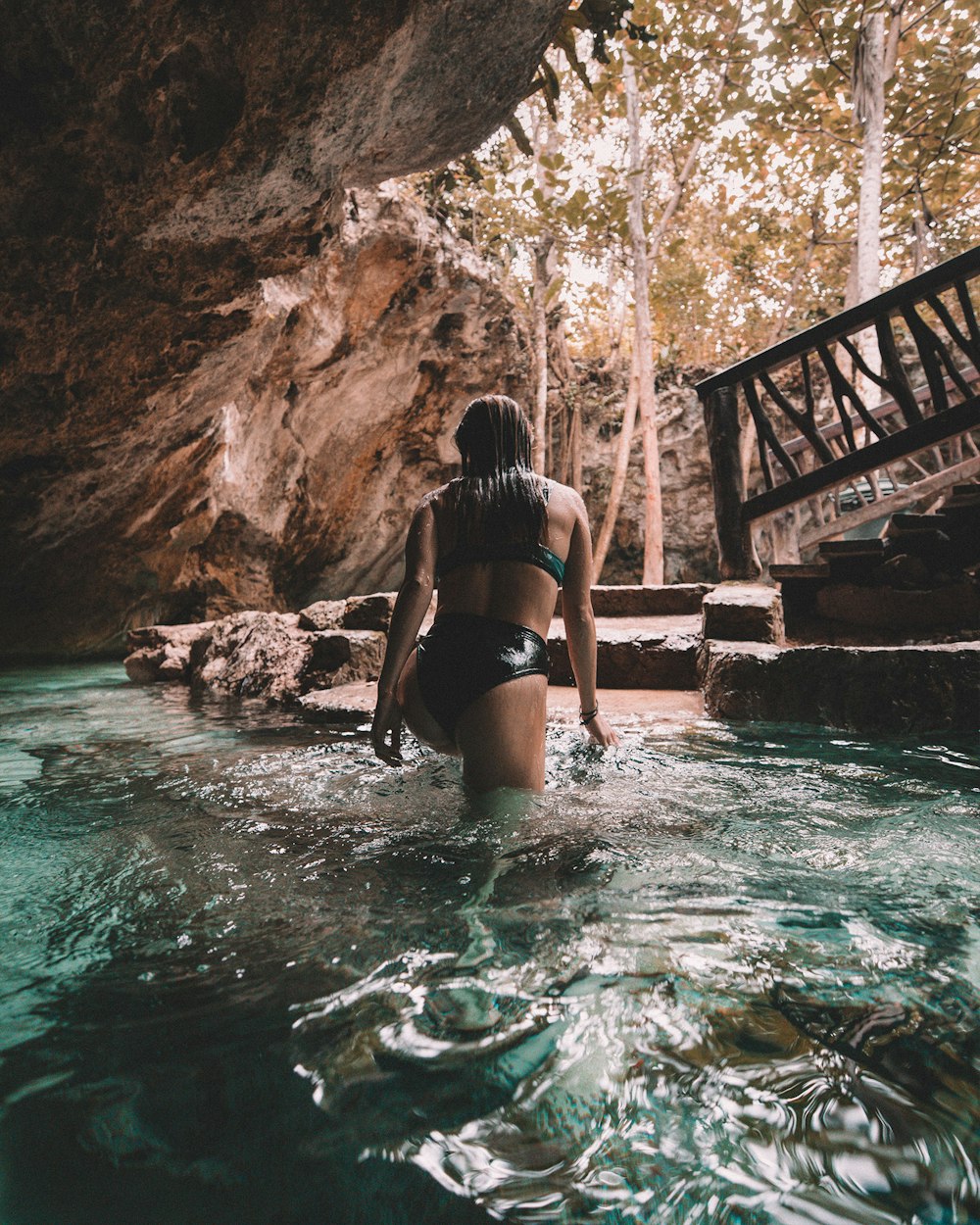 woman in bikini walking out of water inside cave