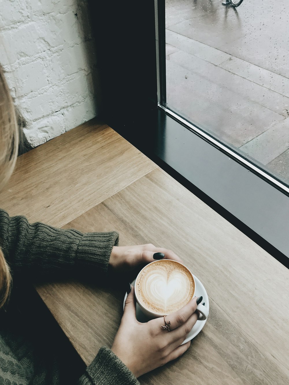 person holding cappuccino on brown wooden desk