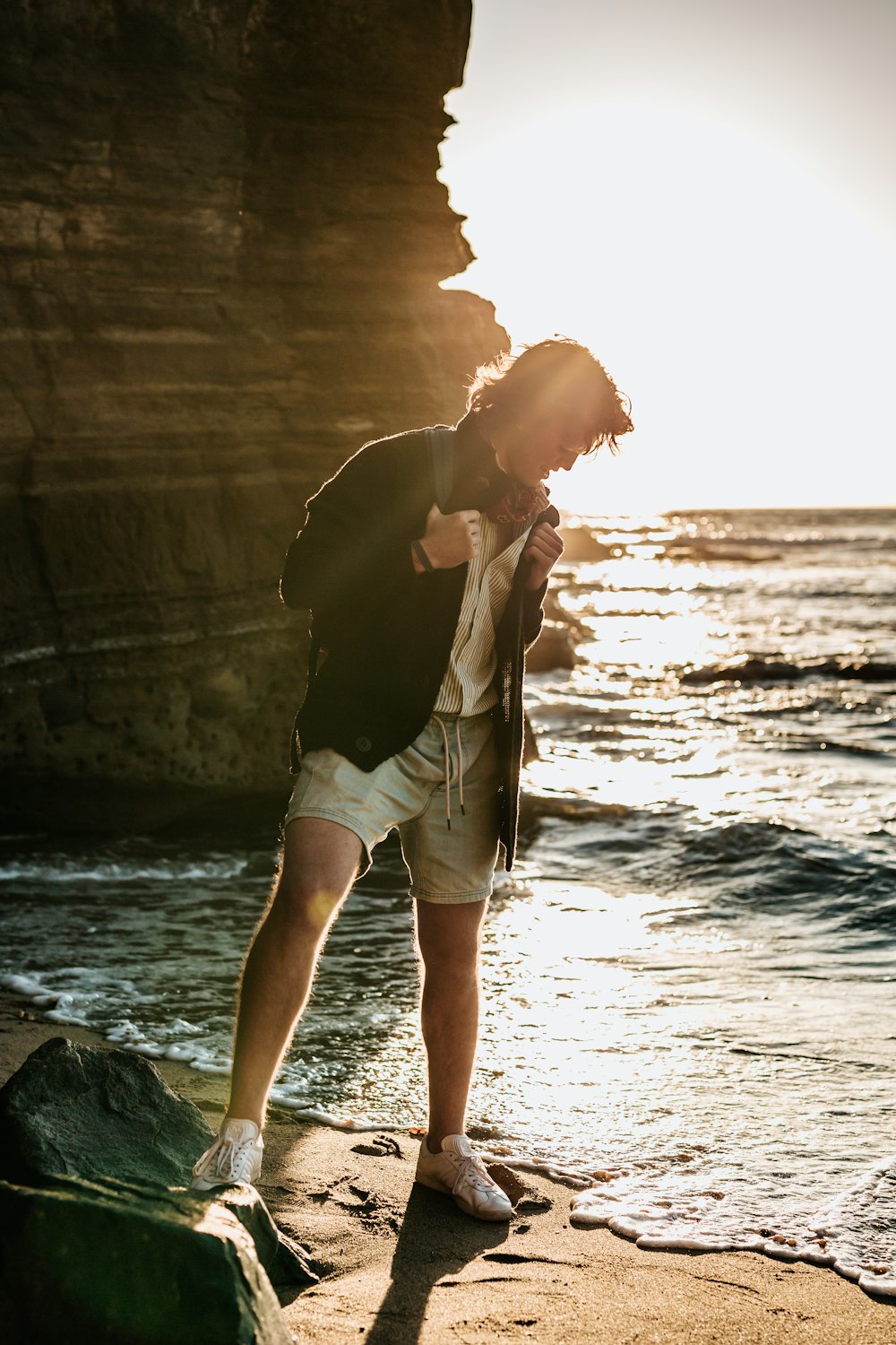 man standing on seashore near rock formation during daytime