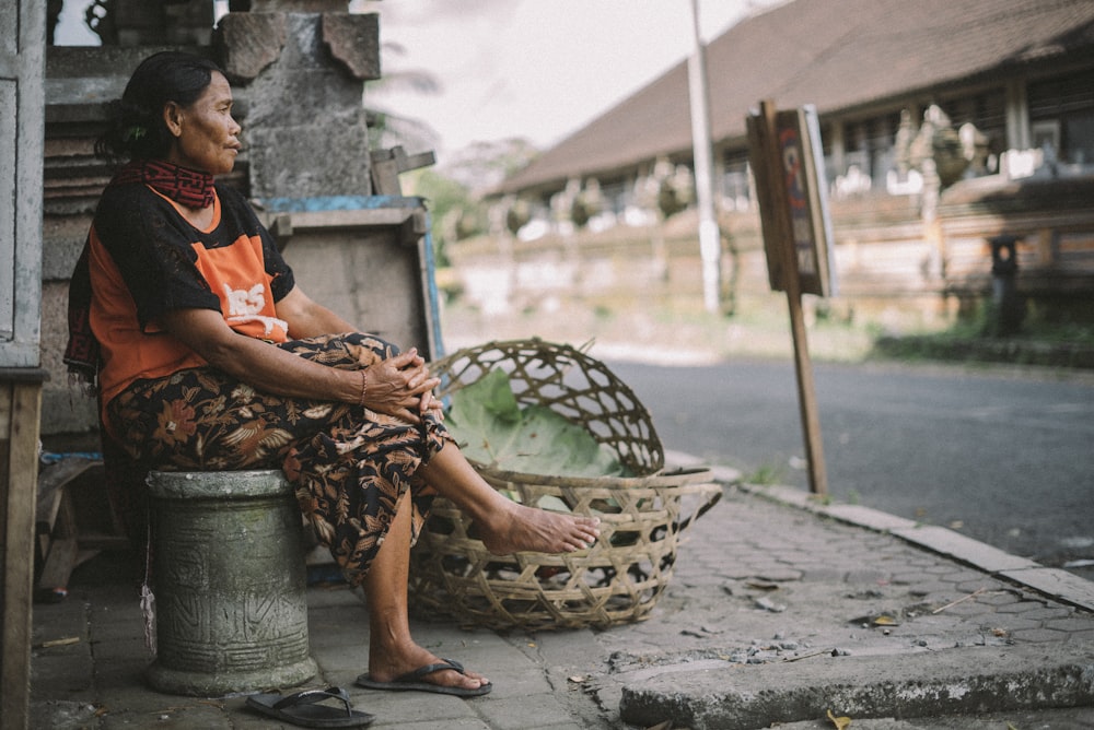 woman sitting on gray concrete chair near brown basket beside road during daytime