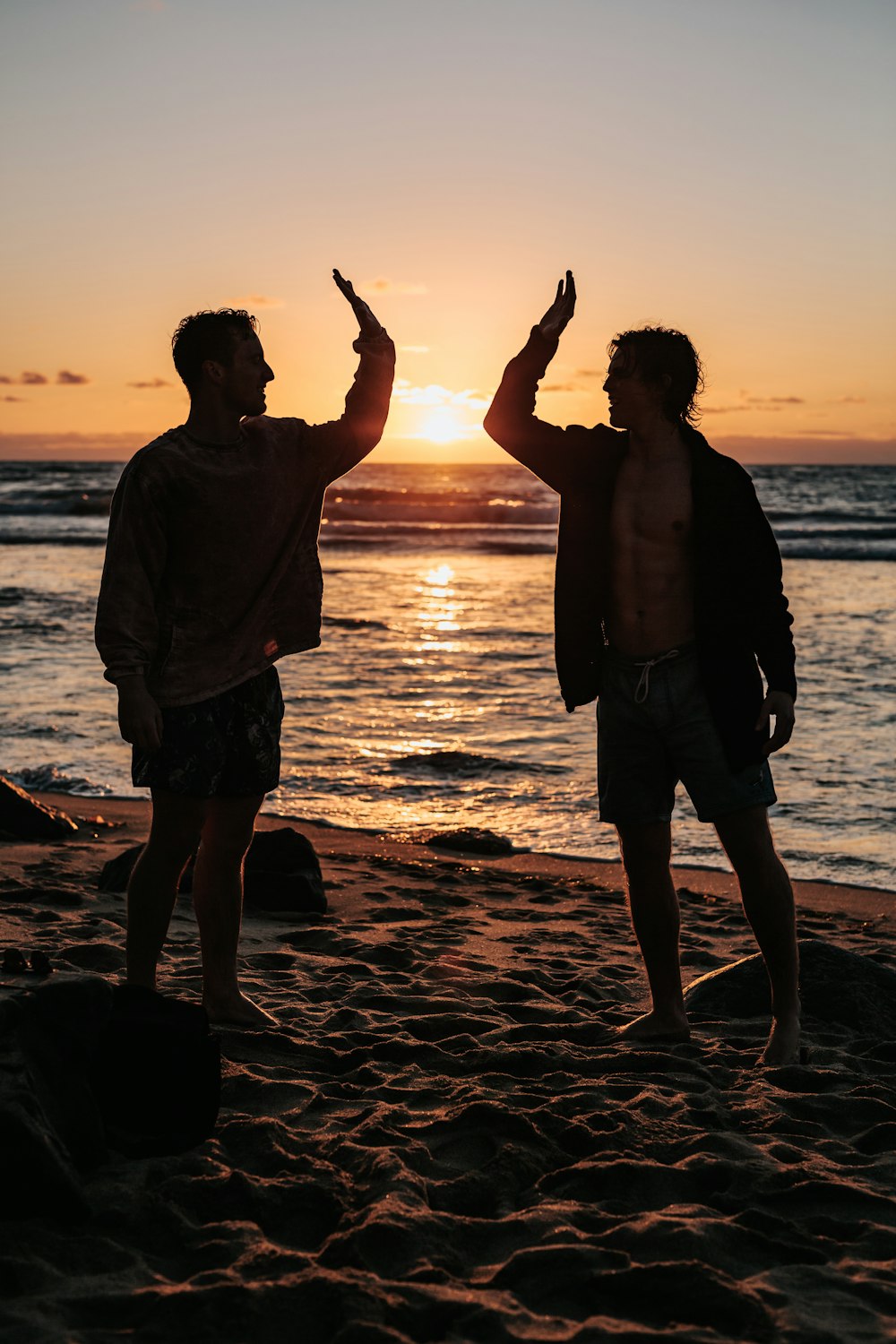 Silueta de dos hombres cerca de la orilla del mar cerca de chocar los cinco durante la puesta del sol