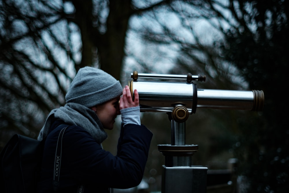 persona che guarda il telescopio sotto gli alberi durante il giorno