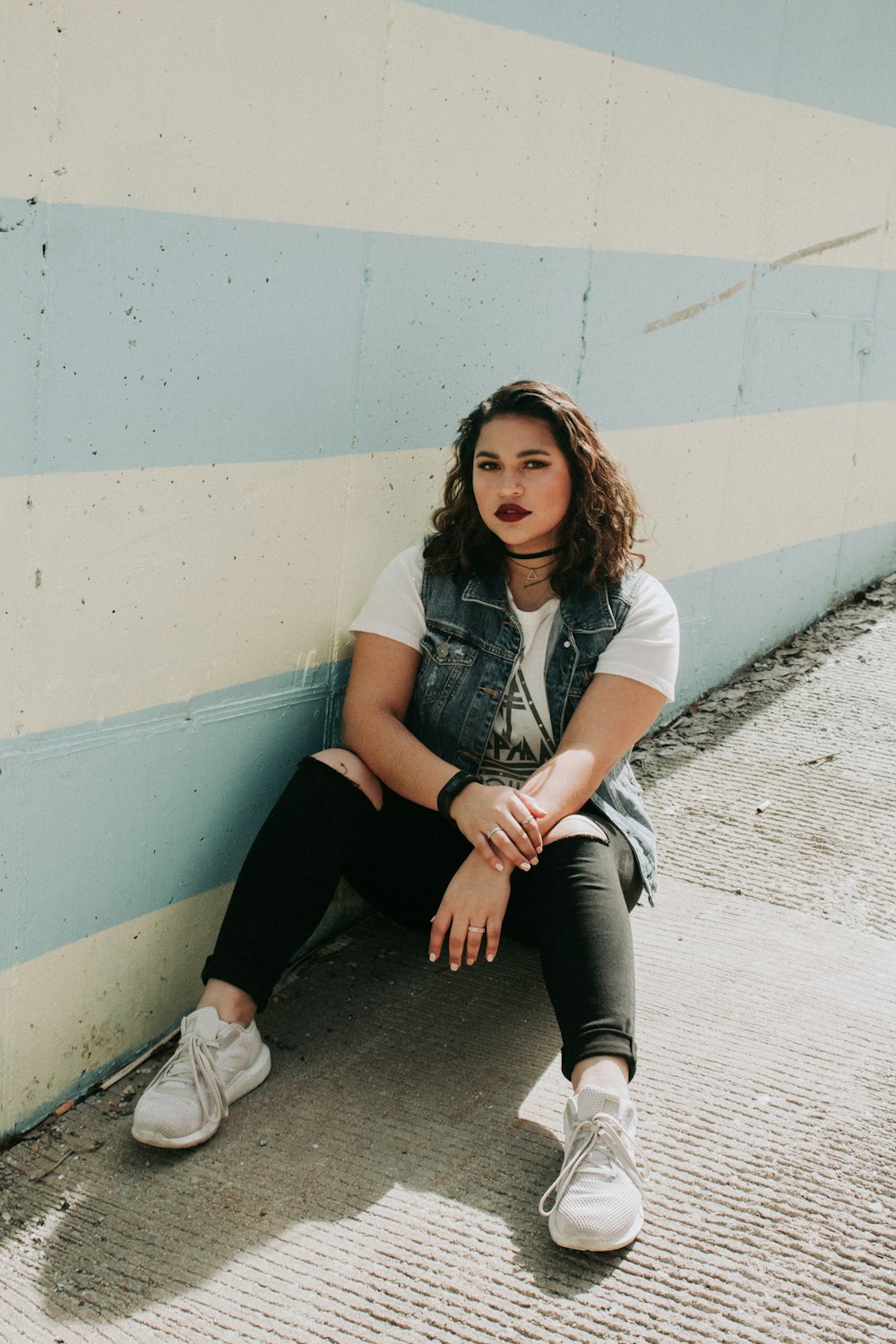 woman sitting on concrete ramp near white and blue wall