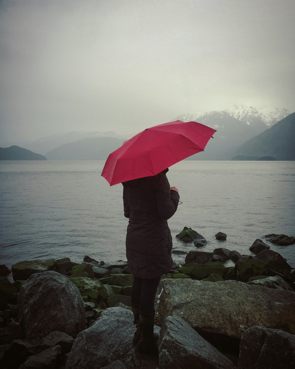Frau mit rotem Regenschirm, die auf Felsen steht