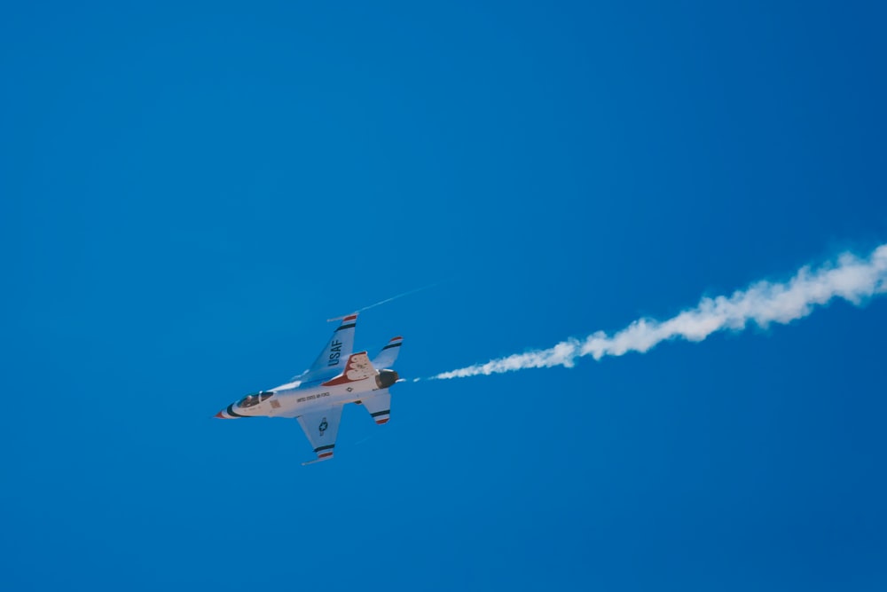 white and blue jet flying under clear blue sky