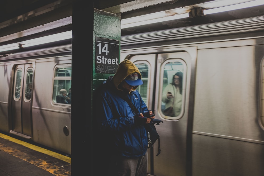 man in blue hoodie using smartphone in train station with train nearby