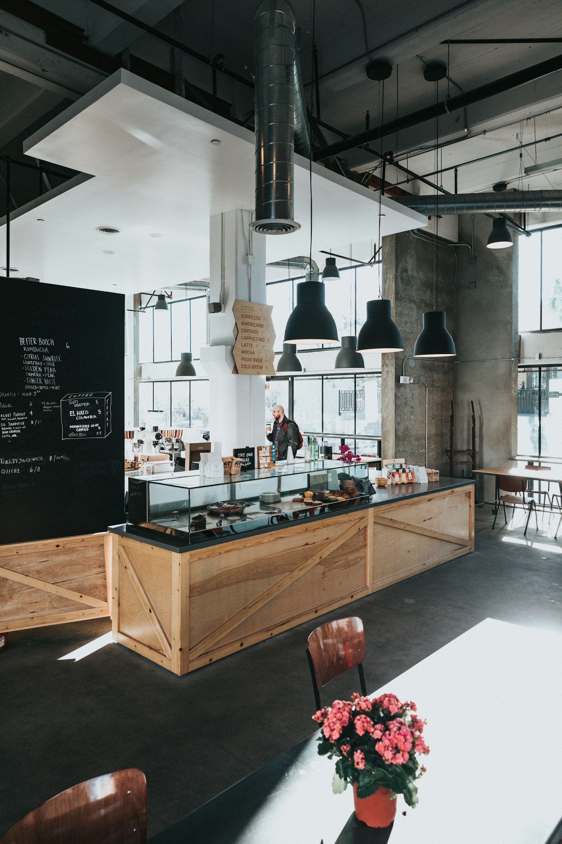 A vibrant daytime shot capturing the café’s chic interior with natural light pouring through large windows, highlighting fresh pastries and latte art on the counter.