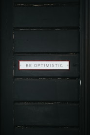 black wooden door with be optimistic text overlay