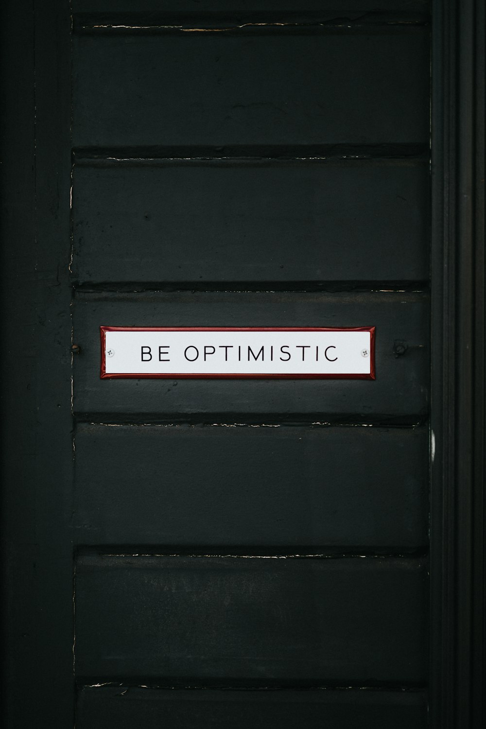 black wooden door with be optimistic text overlay