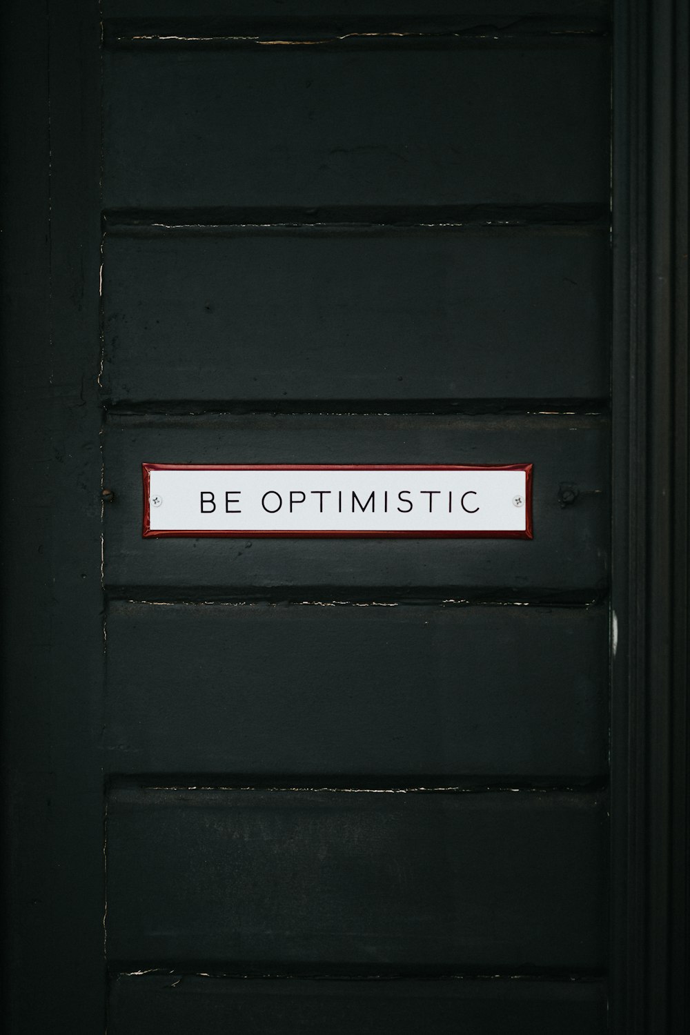 Puerta de madera negra con superposición de texto Be Optimistic