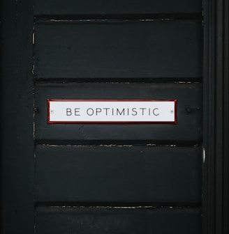 black wooden door with be optimistic text overlay
