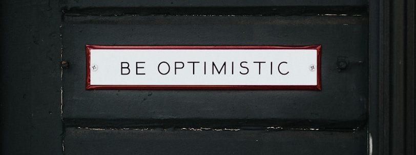 black wooden door with be optimistic text overlay