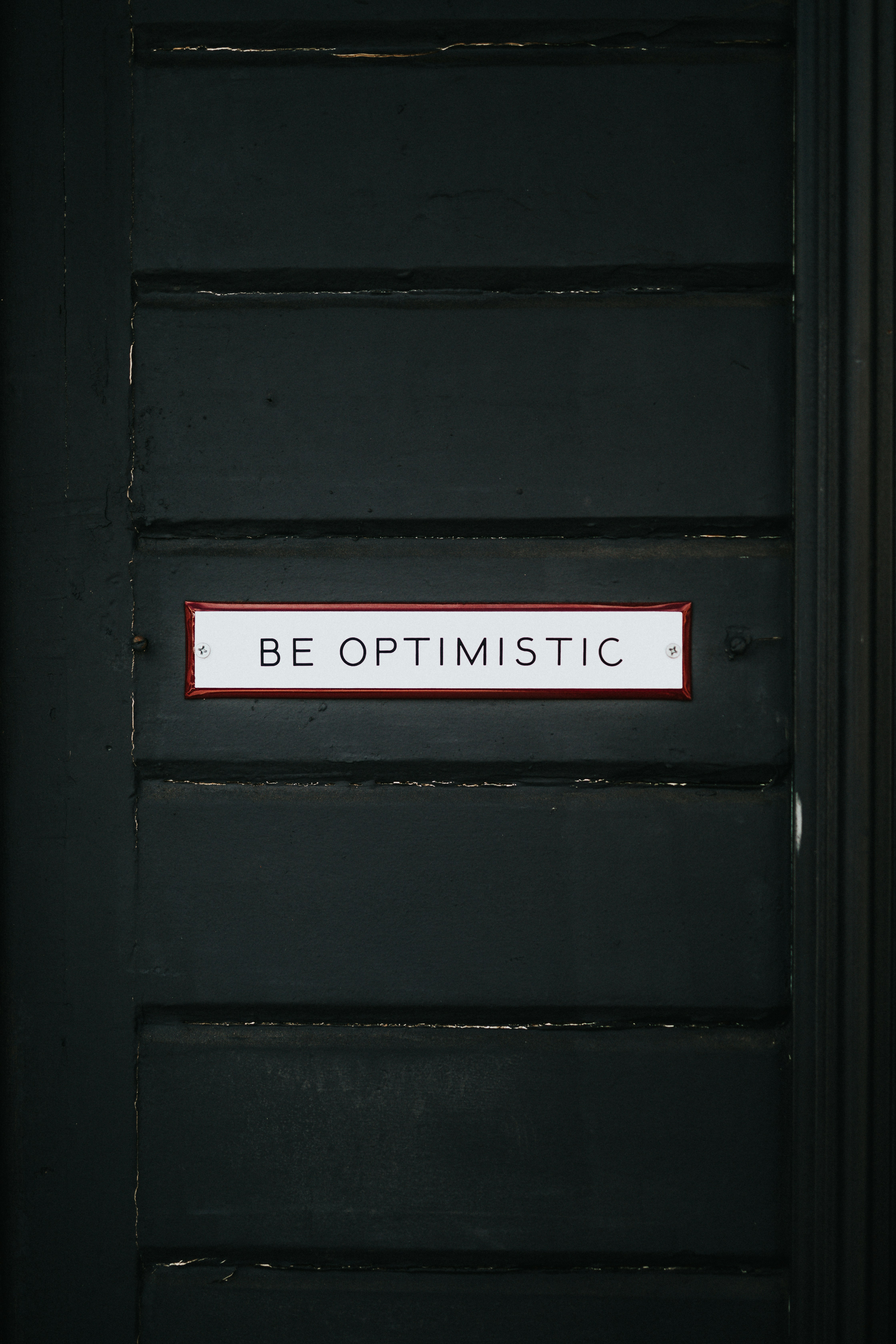 black wooden door with be optimistic text overlay