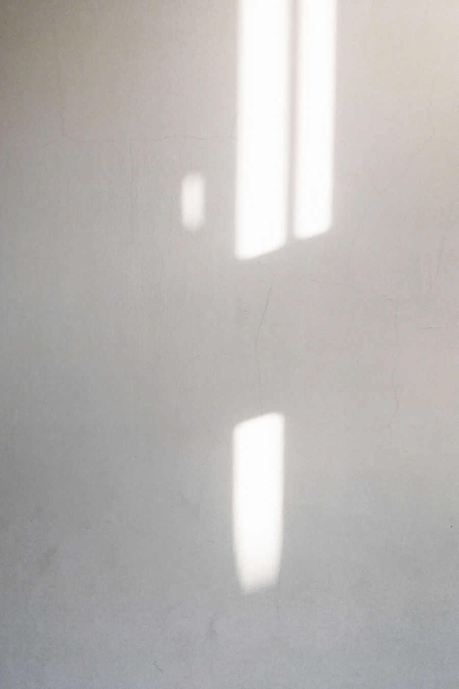Two narrow bars of sunlight falling across a pale plaster wall