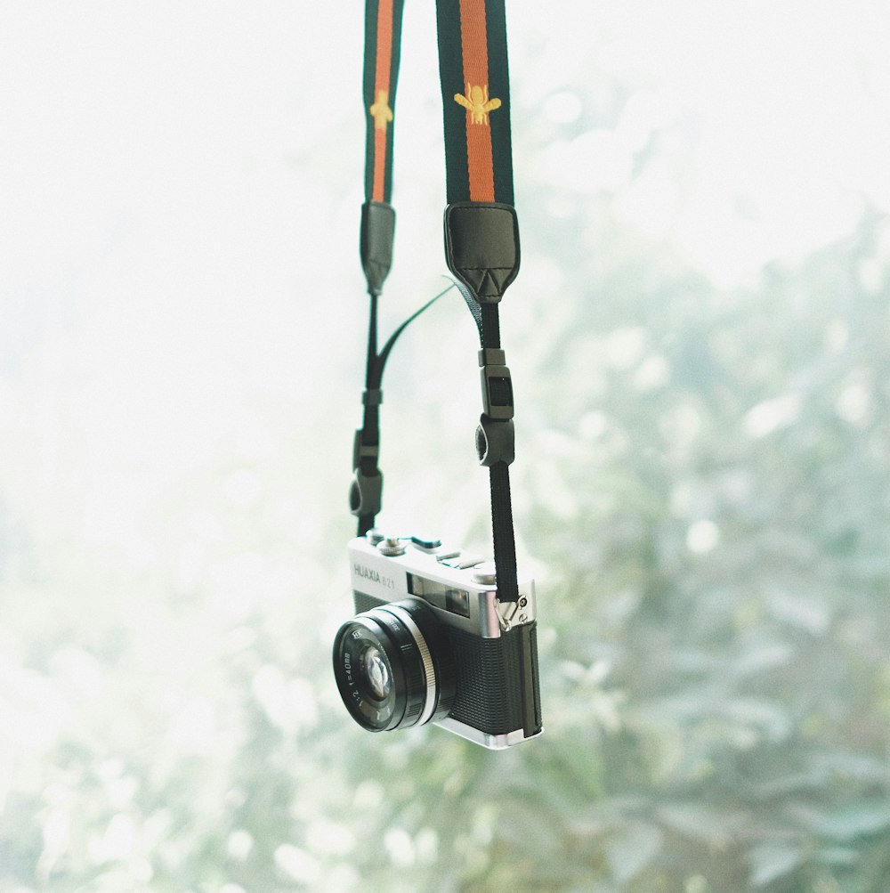 fotografia con messa a fuoco selettiva della fotocamera DSLR nera e grigia appesa